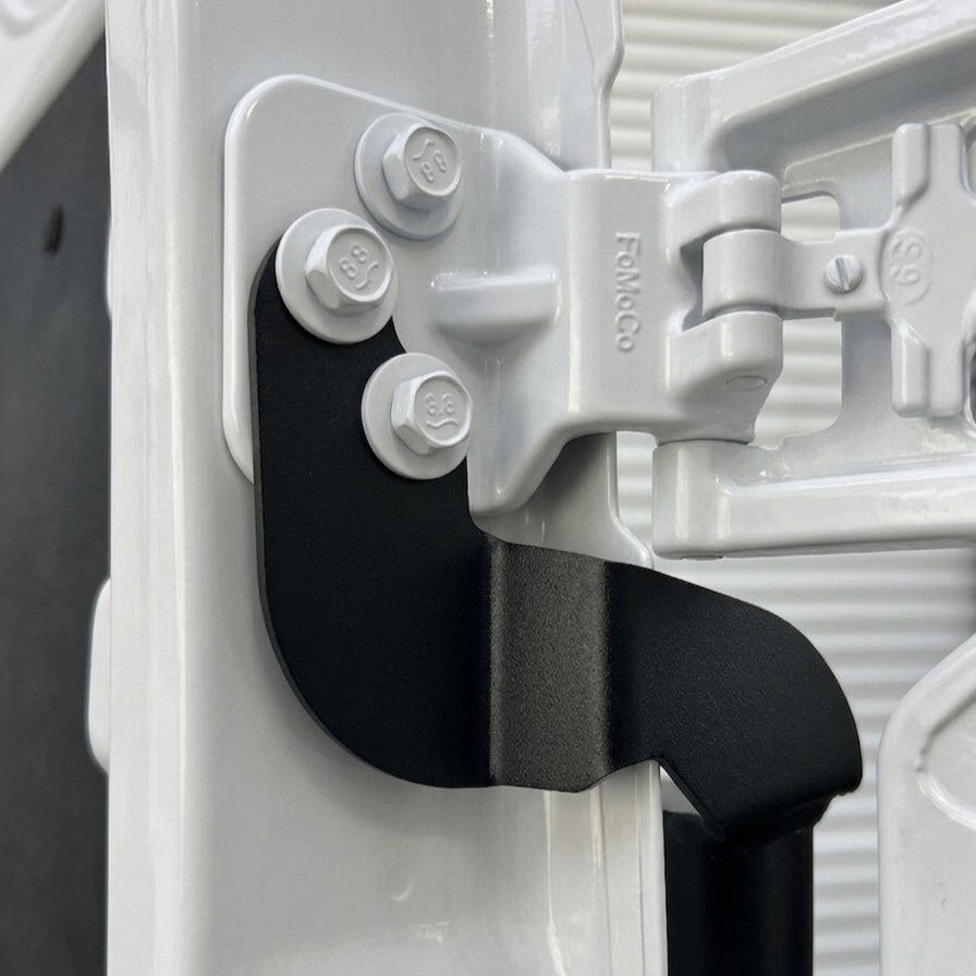 Close-up of Surco TF300 black tire carrier mounting detail on Ford Transit upper driver-side rear door hinge Close-up of Surco TF300 black tire carrier mounting detail on Ford Transit upper driver-side rear door hinge